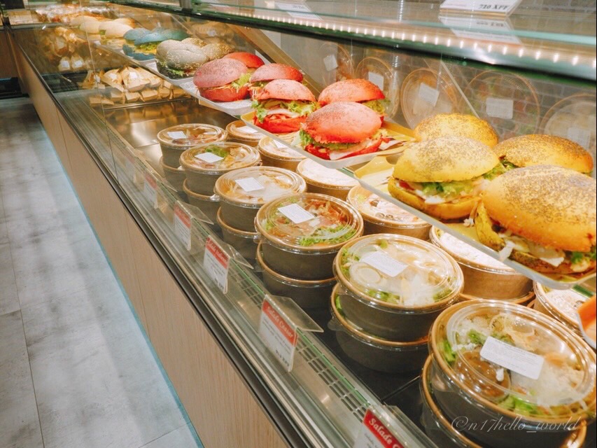A colorful display case of burgers and salads at the bakery L’Atelier Gourmand
